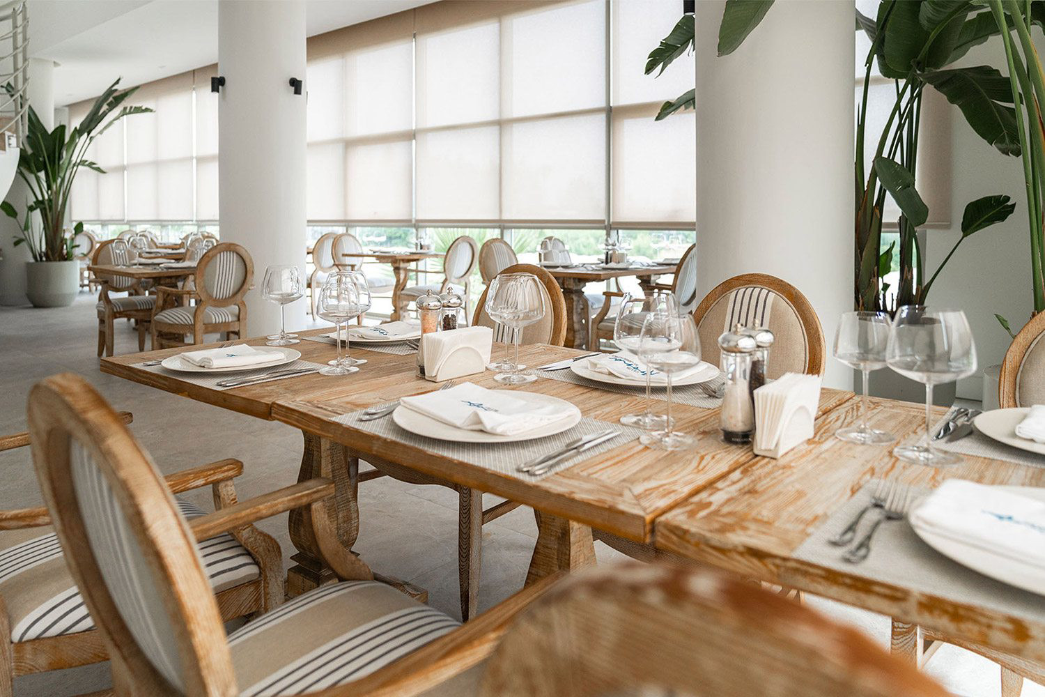Set dining tables, striped chairs and plants inside Frangipani Restaurant