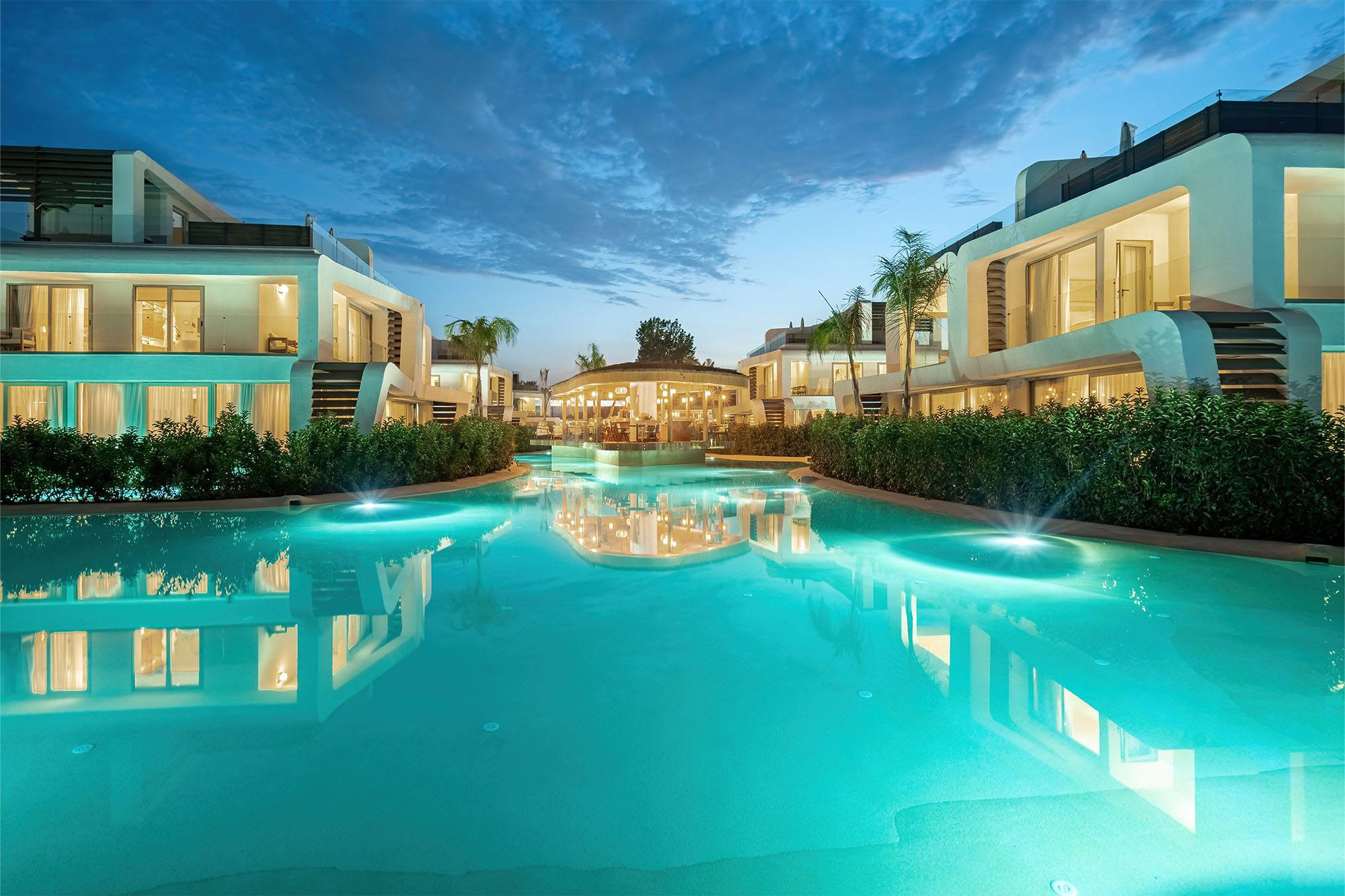 Illuminated villas and central pavilion across water at Club Arona at dusk